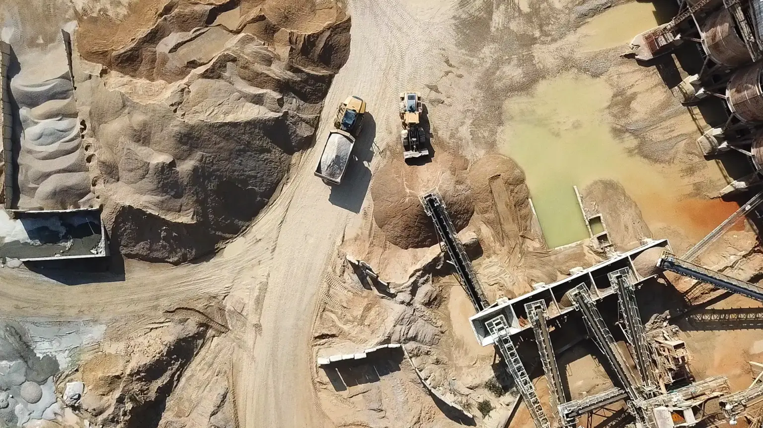Aerial view of heavy machinery and conveyor systems operating in a sandy quarry with stockpiles of material.