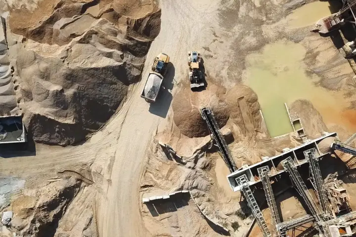Aerial view of heavy machinery and conveyor systems operating in a sandy quarry with stockpiles of material.